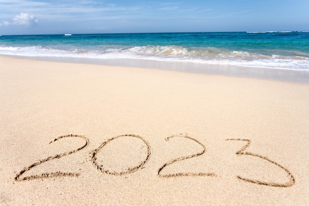 Happy New Year 2023 lettering on the beach with wave