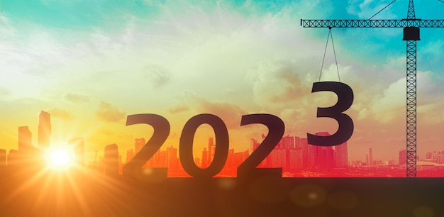 Happy new year 2023 Silhouette of city and construction to create business lifting crane 2023 on sunrise background 2023 preparation