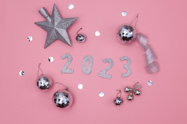 Photo happy new year 2023. silver numbers with festive sparkling ornaments on pink background