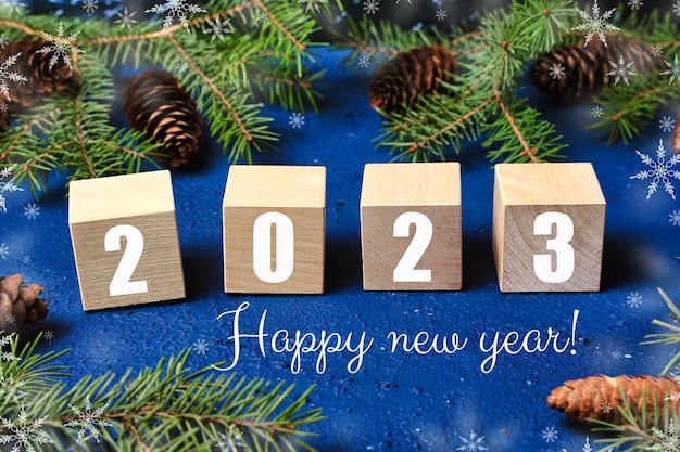 Happy new year 2023 text sign on wooden cubes with frame of christmas tree branch and cones on red background Snowflakes