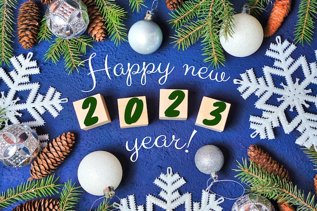 Happy new year 2023 text sign on wooden cubes with frame of christmas tree branch and cones on red background Snowflakes