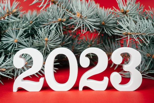 Happy New Year 2023 White wooden numbers 2023 stand with Christmas tree branches on red background Merry Christmas