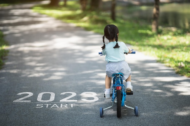 Happy new year 20232023 symbolizes the start of the new year The letter start new year 2023 on the baby girl cycling bicycle on road in nature park garden Goal of Success Number 2023 wallpaper