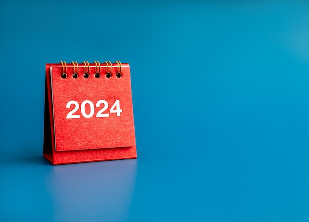 Happy new year 2024 banner background 2024 white numbers year on red small desk calendar cover standing on blue background with copy space Business goals plan and success schedule concepts