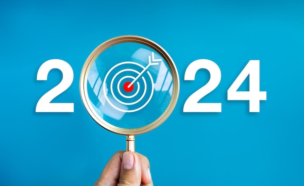 Happy new year 2024 with business concept banner The big white 2024 year number with target dart icon inside the golden magnifying glass in hand on blue background Trends plan and goals concepts