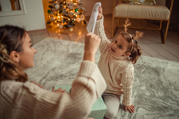 Happy New Year family traditions young mother and her daughter have fun at home near the Christmas tree and fireplace