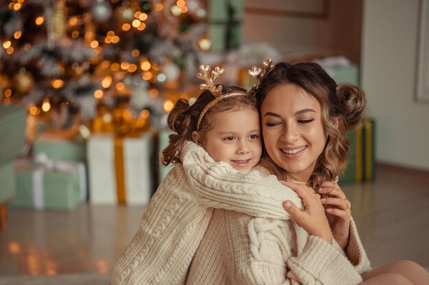 Happy New Year family traditions young mother and her daughter have fun at home near the Christmas tree and fireplace