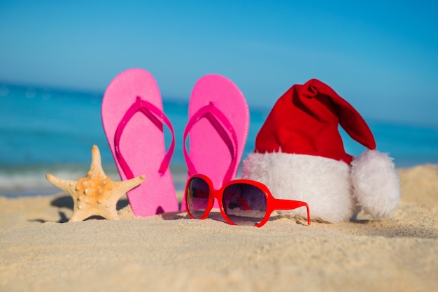 Happy  New Year holidays and Merry Christmas at Sea. Sandals, sunglasses and santa hat on sandy beach.