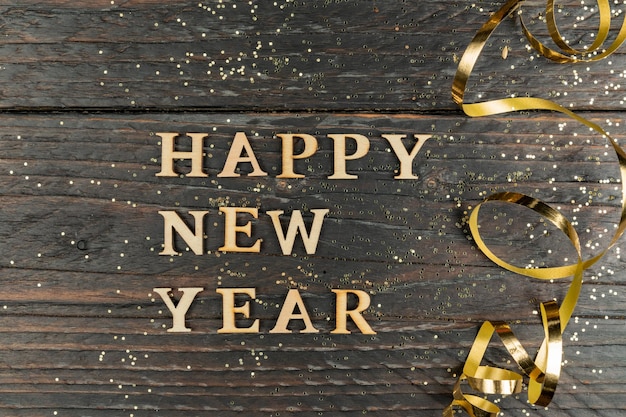 Happy new year inscription made with wooden letters decorated festive golden serpentine on wooden background wih copy space Greeting card for new year celebration