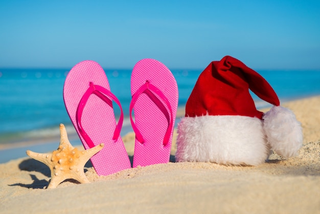 Happy  New Year at Sea. Sandals and santa hat on sandy beach - christmas holiday concept