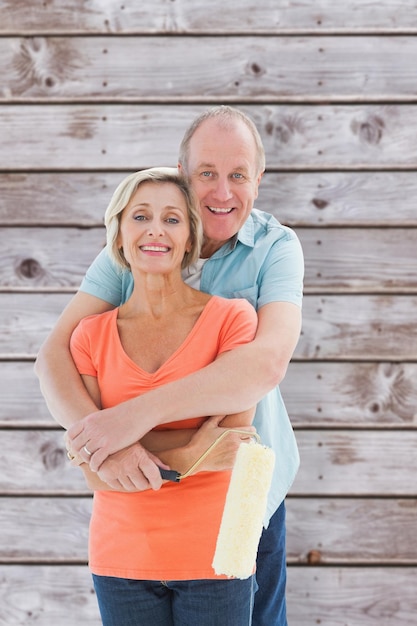 Happy older couple holding paint roller against wooden planks