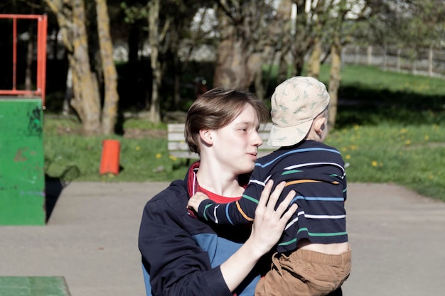 A happy older teenage brother holds his little cheerful brother in his arms