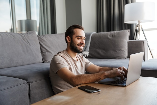 a happy optimistic young man indoors at home using laptop computer.