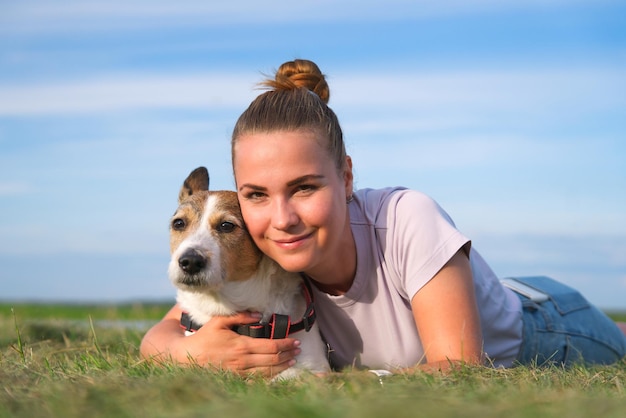 Happy owner young woman beautiful girl with her dog lying on green grass in park, hugging pet