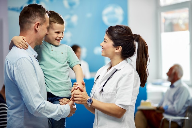 Happy paediatrician talking to a small boy who came with his father in the hospital