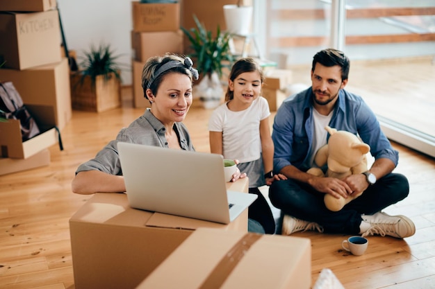 Happy parents and daughter using laptop at their new home