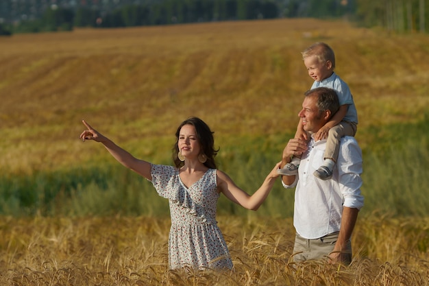 Happy parents and kid walking through a wheat field. Mother, father and little boy leisures together outdoor. Family on summer meadow