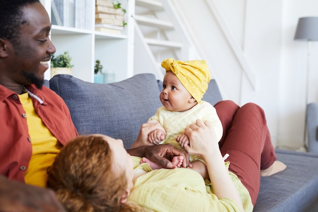 Happy parents playing with their baby girl while resting on sofa in the living room