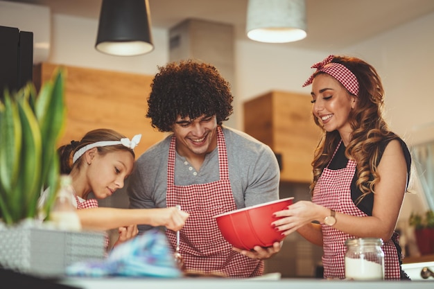 Happy parents and their daughter are preparing cookies together in the kitchen. Little girl helps to her parents to put chocolate dough into molds.