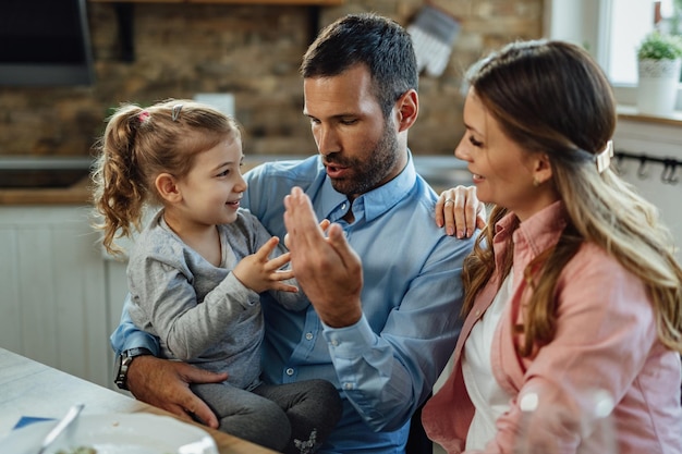 Happy parents and their small daughter having fun while sitting at dining table and communicating.