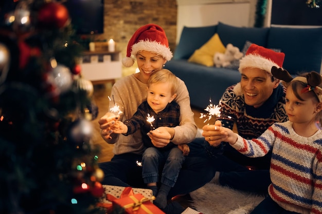 Happy parents and their small kids using sparklers while celebrating on Christmas eve