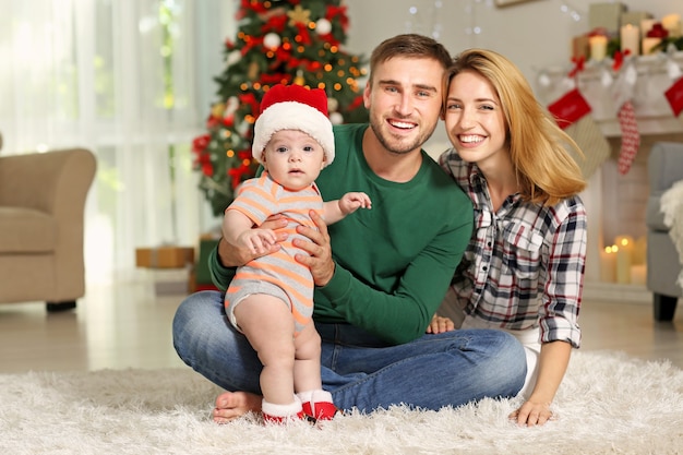 Happy parents with baby in decorated room for Christmas