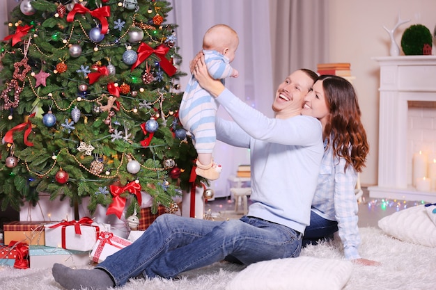 Happy parents with baby near Christmas tree on the floor in the decorated room