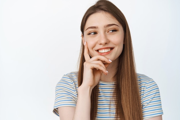 Happy people. Close up of young woman smiling aside, looking thoughtful at copy space, standing on white.