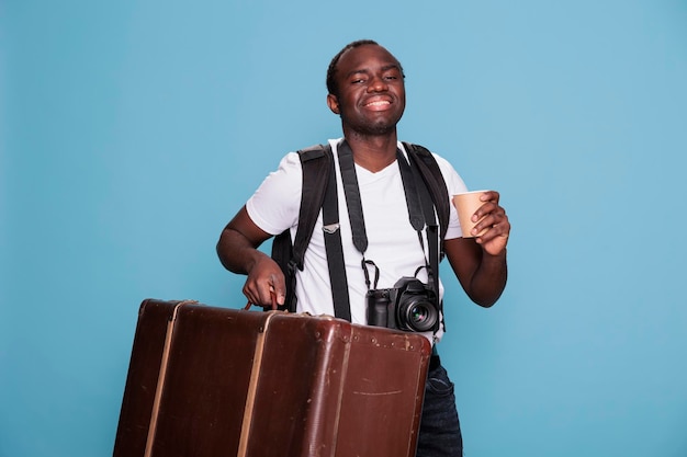 Happy photography enthusiast with luggage and DSLR camera getting ready for holiday journey departure. African american photographer having baggage, backpack and photo device ready for citybreak.