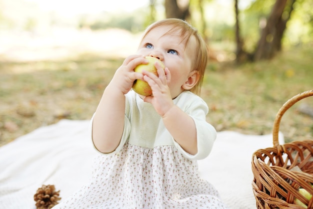 Happy playful child outdoors in autumn park eating apple