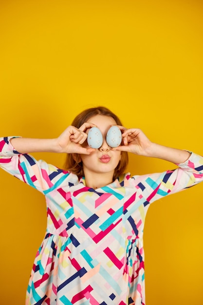 Happy playful teenager girl holding painted Easter eggs covering eyes