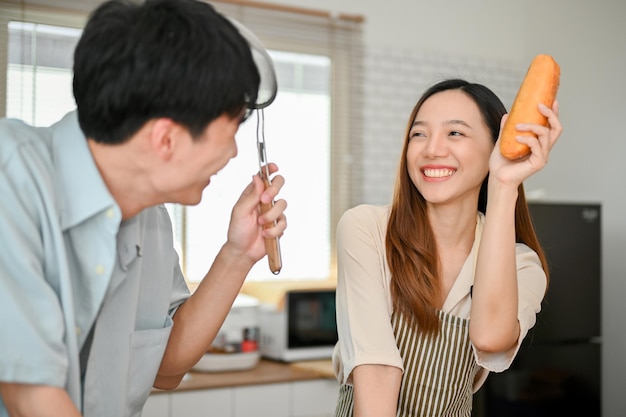 Happy and playful young Asian couple having a fun time while cooking in the kitchen together