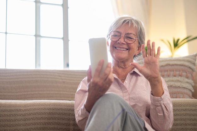 Happy pleasant senior woman relaxing sitting on the floor holding smartphone in hands Smiling mature lady chatting in social networks watching funny videos using mobile applications at home