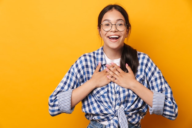 happy pleased emotional cute teenage girl in glasses posing isolated over yellow wall .