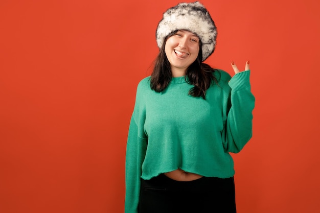 Happy plus size positive woman. Happy body positive concept. I love my body. Attractive overweight woman posing on camera in the studio on a colored background. Girl wearing a sweater and a winter hat