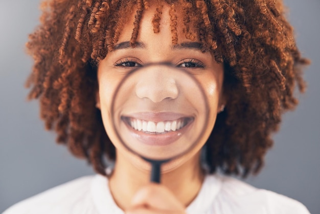 Happy portrait and black woman with magnifying glass in a studio for a investigation or research Happiness smile and portrait of a young African female model with a zoom lens by a gray background