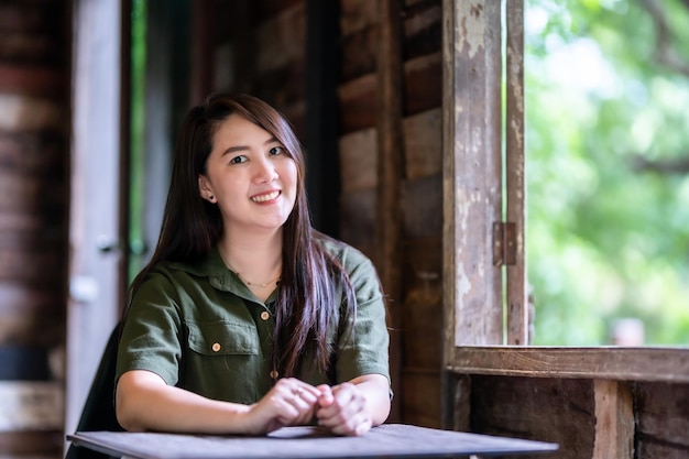 Happy of Portrait Happy Smiling beautiful Asian woman wearing brownish green dress stylish hipster with beside the window of a wooden house background