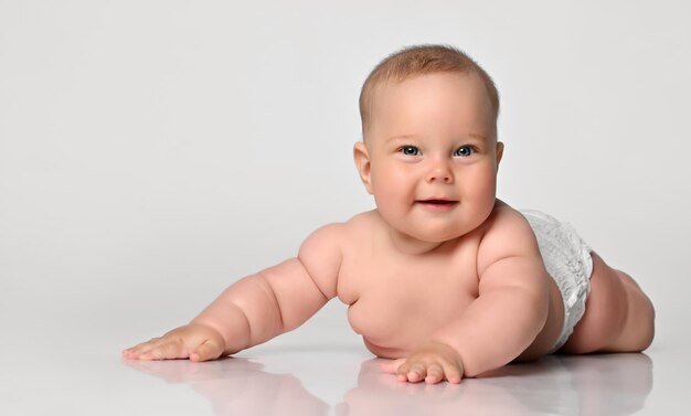 Happy portrait Six month old baby girl in a diaper lying sly looking at you arms outstretched to the sides on white background