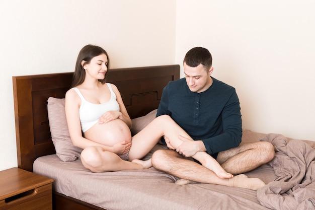 Happy pregnant family Husband massaging his pregnant wife legs and sitting together on couch in their home