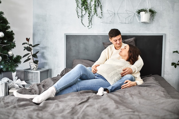 Happy pregnant family is lying on the bed at home. He plans a family life in anticipation of the baby. Family happiness, the birth of a child.