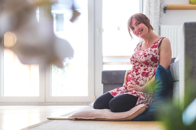 Happy pregnant mother is sitting on the floor hugging her tummy