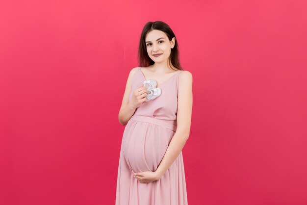 Happy pregnant woman holding baby girl booties against her belly at Colored background Happy pregnancy Copy space