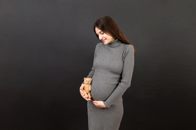 Happy pregnant woman holding a teddy bear against her belly at Colored background Young mother is expecting a baby Copy space