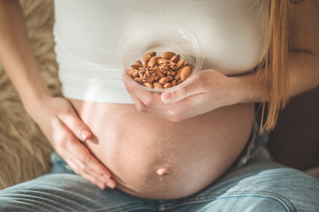 Happy pregnant woman at home eating fresh nuts - almonds, walnuts. Healthy pregnancy concept.