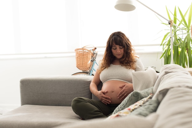 Happy pregnant woman sitting and touching her belly at home