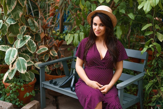 Happy pregnant woman in a straw hat sits on a bench in a Park