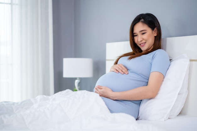 Happy pregnant woman stroking her belly on a bed