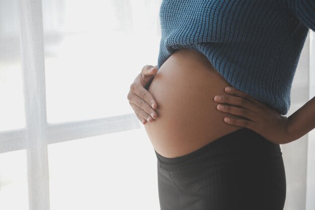 Happy pregnant woman touching belly in front of white wall