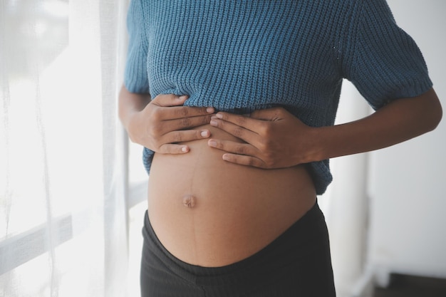 Happy pregnant woman touching belly in front of white wall