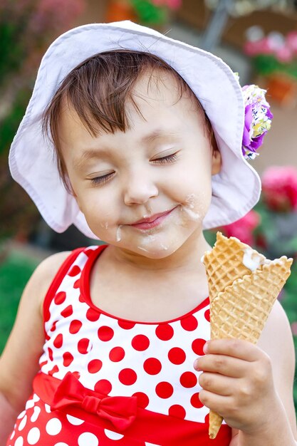 Happy preschool girl eating colorful ice cream in waffle cone on sunny summer day